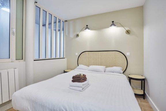 Chambre minimaliste avec tête de lit en rotin et verrière blanche